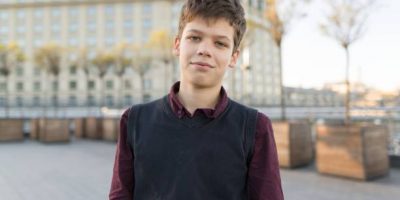 Outdoor portrait of smiling teenager boy 14, 15 years old. City background, golden hour